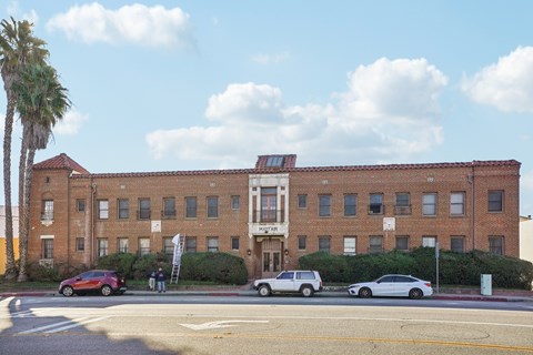 A red car is parked on the side of the road in front of a brick building.
